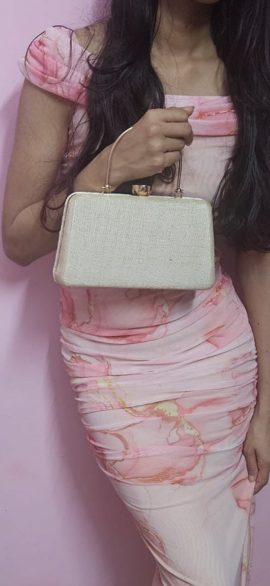 Person wearing a floral dress holding a white handbag against a pink wall.